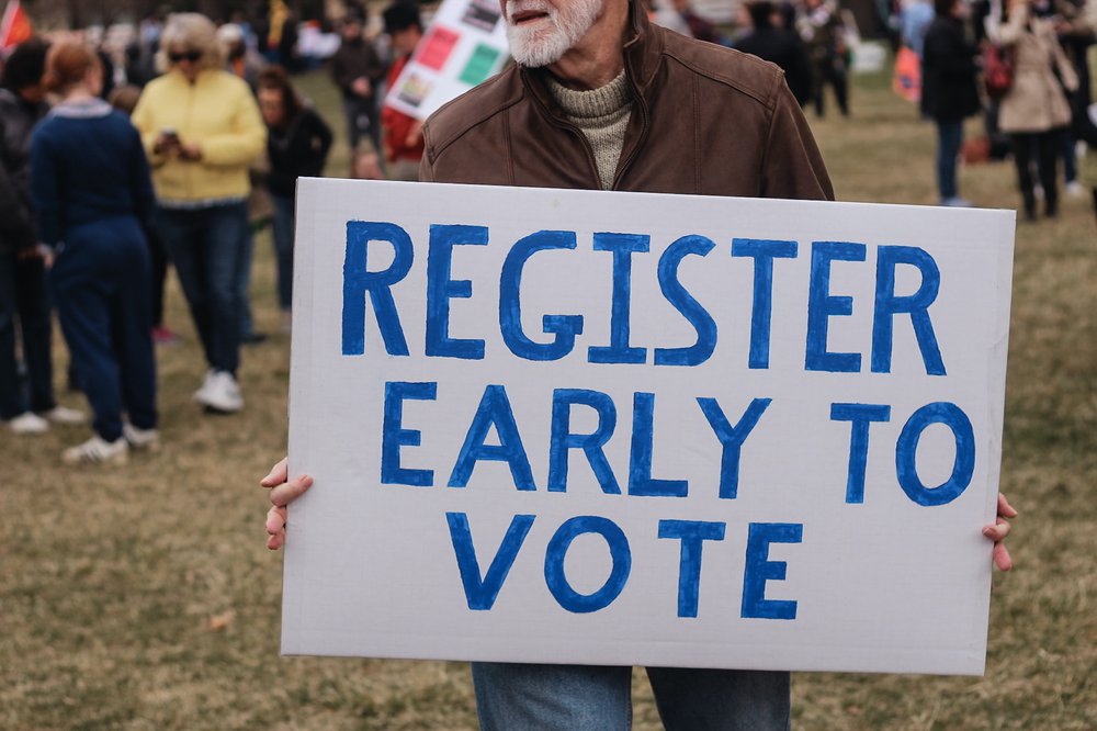Man holding sign that says Register Early to Vote